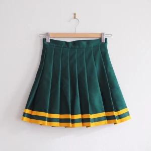  - Mörkgrön, veckad cheerleaderkjol med gula ränder nedtill från Americana Classic Vintage. 