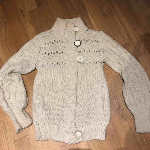  - Stickad kofta med både tryckknapp och stora dekorations- knappar. I ull.  