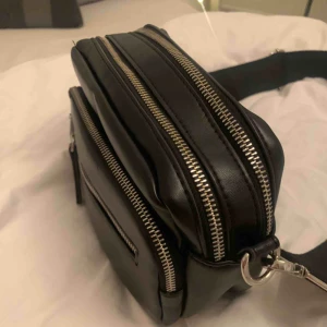  - Svart väska med flera fak och ett tjockt band 