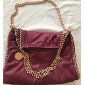 Stella McCartney  - Vinröd med guldiga kedja, det är den stora modellen! Köpte den på Plick i våras men säljer för att den inte kommer till användning längre. Den har inga slitningar utan är i fint skick. Äkthetsbevis medföljer! 