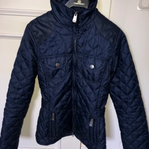 Höstjacka - Höst/vårjacka. Marinblå med detaljer. Bröstfickor, fickor fram med dragkedja, ”knittat” material. Justerbart skärp i två olika lägen. Strl. XXS men sitter som XS/S. Superfint skick.