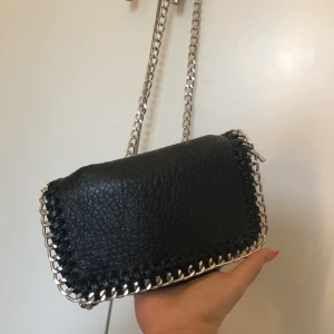 Axelremsväska - Axelremsväska från Tiamo i väldigt bra skick, inga slitningar. Svart väska med skinnimitation med silvriga detaljer.