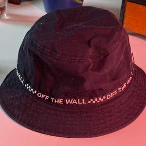 En svart bucket hat från vans med texten ”off the Wall” runt hela. Den har även en liten detalj på insidan som ni ser på andra bilden 