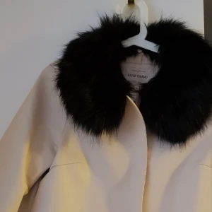  - Snygg ljus beige jacka med pälskrage. Materialet är i 100% polyester. Liknande skinn imitation. (fattas en knapp).  Pris exkl. frakt