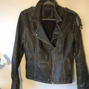  - MC inspirerad  skin jacka i äkta skin, jackan är ganska tjock och rejäl, har en detalj över ena axeln som går att byta plats på eller ta bort helt. Jackan är köpt på en mässa för något år sedan. Men den är aldrig använd. 