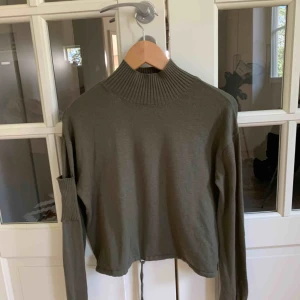  - Något croppad stickad tröja med knytning i midjan och ficka på axeln. 