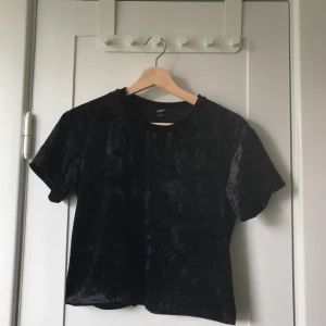 Svart t-shirt Monki sammetseffekt - Svart t-shirt från Monki i sammets-/velourliknande material. Något croppad. Storlek: XS.