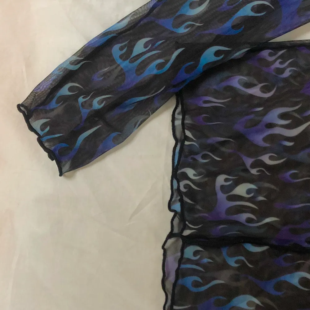 En svart transparant mech-tröja med ett mönster av blå och lila eldflammor💙stretchigt material💜använd ett fåtal gånger så i väldigt bra skick💙 lite halvt volangiga kanter💜 frakt ingår ej utan kostar 42kr💙 säg till om det finns några frågor💜. Toppar.