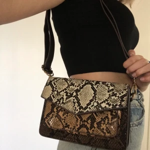 Väska - Jättesöt väska som jag säljer för att det inte riktigt är min stil🥰🥰  Väskan har ormmönster i olika bruna nyanser!! Bandet går att justera. Köpare står för frakt!!!❤️❤️