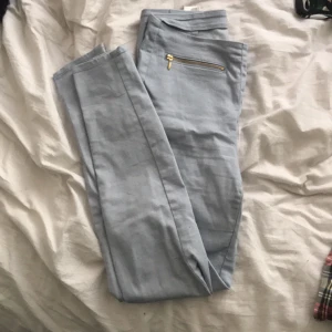  - Ljusblå byxor med guld dragkedja. Knäppning i sidan.