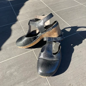 Klackskorna i toffelmodell - Klackskor av märket Emma. Svart läder med sula av gummi. Lätta att bära. Storlek 40 (normala i storleken). Om de ska skickas med posten tillkommer fraktkostnad. 