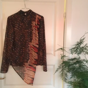  - Fin, oanvänd omlottblus i brun/svart mönster. Snygg till långbyxor eller kjol, vardag eller fest. Nypris 899kr. Märke Vintage By Fé.