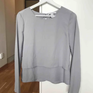  - Grå i 100% polyester från NLY Trend. Dekorativt dubbeltyg fram, knäppning i nacken.