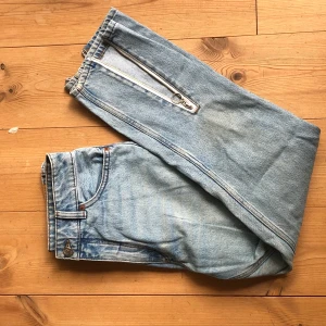 Jeans  - Ljusa jeans med slitsar/dragkedjor nedtill. Köparen står för frakt 