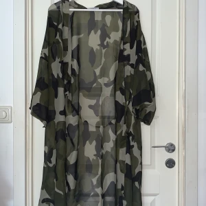 Kimono/Cardigan - Kimono i militärmönster. Storlek ONESIZE. Den går ner till mitten av vaderna på mig och jag är 163 cm. Knytband finns med. Aldrig använd.