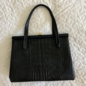 Vintageväska, svart krokodilimitation - Supersnygg vintage väska i svart krokodilimitation. I bra använt skick förutom någonting klottrat på insidan, se bild. Mått 20x26. Kan hämtas upp i Malmö/Lundområdet alt 49 kr för frakt!