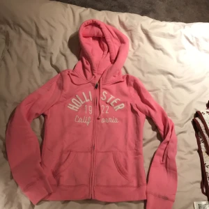 Hollister rosa hoodie  - Rosa hoodie från hollister. Köpt för några år sedan men knappt använd och i gott skick. Glittrig logga och finns ”lucka” för hörlurssladd i fickan!