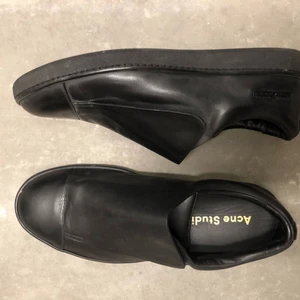  - Skor i herrmodell från ACNE STUDIOS. Som nya, endast använda vid ett tillfälle inomhus (se undersida). Svart läder med kardborrband, svart acnelogga i metall skons utsidan. 