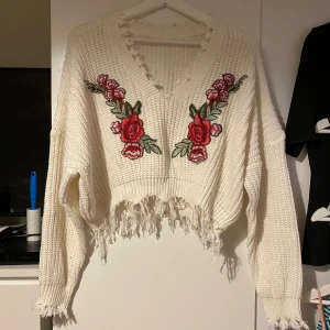 Stickad tröja - Vit stickad tröja med blommor på bröstet. Tröjan är croppad i modellen. Ingen lapp med märke eller storlek men gissar på att det är XL eller oversized L