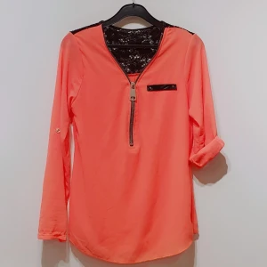 Blus - Fin, tunn blus i korall med spets i ryggen. Ärmarna kan vara långa eller med knapp för att rullas upp