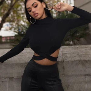 Svart top, korsad vid sidorna - Skön svart top med band vid sidorna som sitter bra mot kroppen. Sitter som på bilden. Använd en gång. Är lite som en croptop. Lite för kort för min smak. 