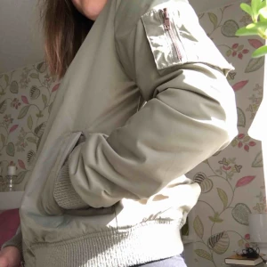  - En grön bomberjacka från Kappahl. Den är orange inuti. Innerfickan är sönder. En ficka på armen med dragkedja. Mönster på ryggen och på ena armen är det en ros. Köpare står för frakt. 