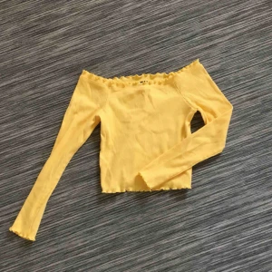  - Helt oanvänd croppad off-shoulder topp från Gina. Materialtet är ribbat och har ”vågiga” kanter. 