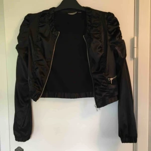  - Svart jacka med glansig utsida och foder inuti. Storlek 170. Köparen betalar frakten