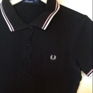  - Svart Fred Perry piké i stl L, men den är mkt liten i storlek så passar S. Kragen har vita/rosa ränder i kanten. Supersnygg och i bra skick, men omsydd till en kortade längd. Möts i Sthlm/fraktar. 