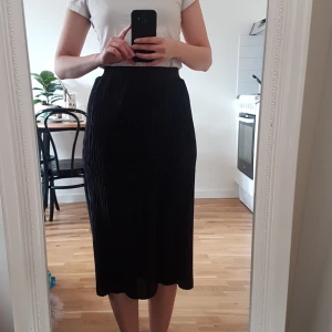 Svart plisserad midikjol - Ny svart/mörkgrå plisserad midikjol i glansigt tyg från Mango Casual i strl. S, gjord av 100% polyester. Frakt är inräknat i priset. Skickar i postens blå påsar och samfraktar gärna. Tar helst emot betalning via Swish. 🌻