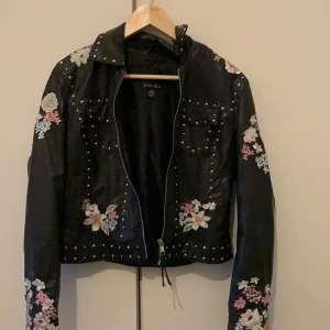 Skinnjacka  - En oanvänd skinnjacka med broderade blommor och nitar på. Väldigt skön och fräch