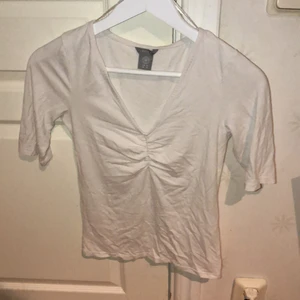 En vit basic topp - Denna topp är både en vardagstopp och någonting du kan ha till festen. Denna topp har en trekvarts ärm och är lite skrynklig vid bröstet, denna tröja är också V-ringad.