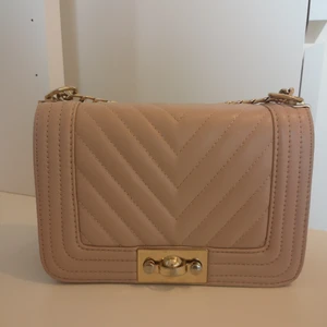 Beige/gammelrosa axelbandsväska - Axelbandsväska med guldkedja. Lite slitage vid knäppningen, se sista bilden. Mått 22x15 cm. Frakt tillkommer. 