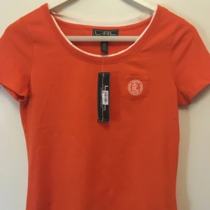  - Ny Ralph Lauren T-shirt (Lauren active) med tagen kvar. Finns dock en liten fläck på framsidan(se bild). Storlek XS men passar en S. Köpt på Macys och säljs pga av att storleken är förliten.