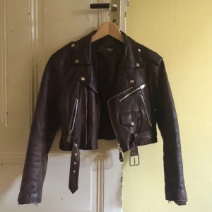  - Skitsnygg brun skinnjacka i klassisk bikermodell. Kortare i midjan så passar perfekt till höga kjolar och byxor! Från London✨står att det är en medium, själv är jag en XS.  Har lite mindre slitningar då den är vintage, skickar bild närmre på dem vid efterfrågan! 💕