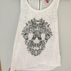  - En vit top med svart dödskalle motiv & dragkedja vid nacken.