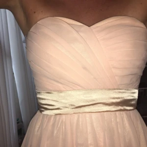  - Superfin ljusrosa långklänning i fint skick. Använd vid två tillfällen. Klänningen är måttbeställd men jag skulle säga att den passar 36/38 då den går att ställa in med knytning i ryggen. Jag är 172 cm lång och hade 10 cm klackar vid tillfället.   Det är några fläckar på tyget nere vid fötterna, men det syns inte när man har den på sig.