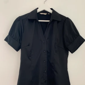 Riley blus - Stilig och välbehållen Riley Woman blus i storleken 38. Kortärmad med något puffiga ärmar. Stängs med knappar och är i silkestråd. Mycket bra skick.