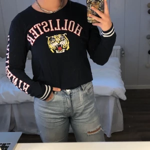 Långärmad T-Shirt Från Hollister - Supersnygg, mörkblå, långärmad tshirt från Hollister med ett tigerhuvud samt text på bröstet. Även text (”california”) på ärmen. Tröjan är använd några få gånger men får tyvärr inte någon uppmärksamhet längre. Nyskick!