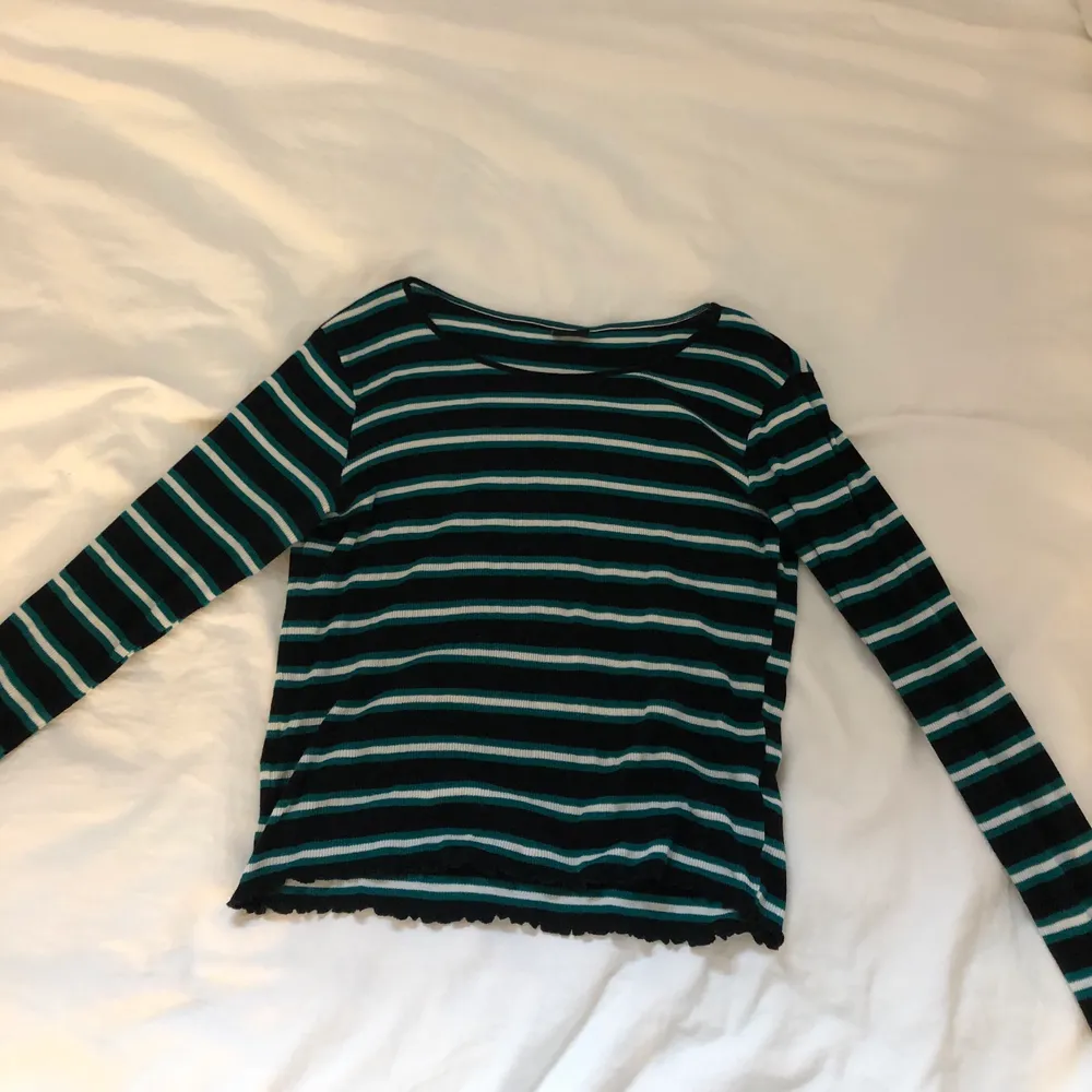 Superfin långärmad tshirt från Gina Tricot som jag köpte för ca 2år sedan. Den är använd några få gånger men är i nyskick! Tröjan är svart med vita och gröna ränder samt har ”volanger” i sömmen längst ut på ärmen och nertill. . T-shirts.