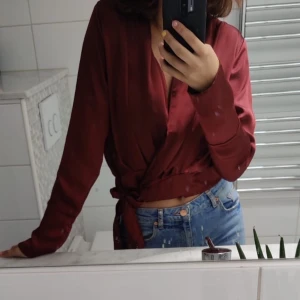 Vinröd blus med knytning  - Jättesnygg vinröd blus med knytning som man kan styla på olika sätt. Har använts i fåtal gånger men ser ut som ny.  