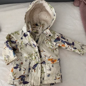 Fin Next vinterjacka - Använd bara få gånger, jackan är varm fodrad i str. 80-86.  Märke Next, vit blommiga mönster med luva. I nyskick. Varm och vattentätt. 