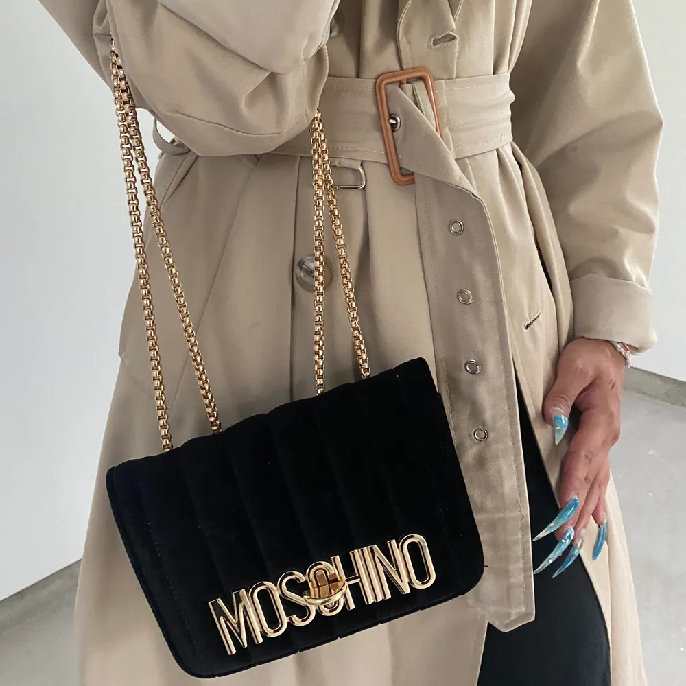 En Moschino handväska i velour-tyg med guldkedja som går att justera efter hur man vill bära upp väskan. Väskan är stabil och har en röd insida av fuskläder och en inreficka. Fraktar för extra kostnad 🦋 (OBS, ej äkta). Väskor.