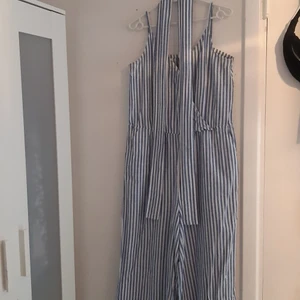 Lindex byxdress strl M - Vit och ljusblå randig byxdress med surplice halsringning som kan knäppas en viss del, vit och ljusblå tygbälte kommer med