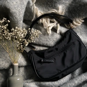 svart axelremsväska - nu säljer jag vidare denna fina väska för att den ej kommer till användning!!🥺 den är köpt här på Plick men är fortfarande i bra skick. den är justerbar och har ”guld” detaljer:) den har ett fack på baksidan och ett litet inuti! den är ca 25x15 cm stor