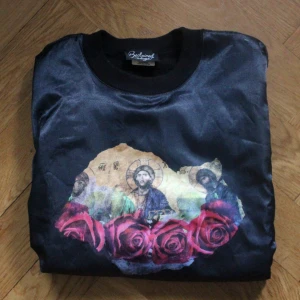  - Cool och udda collegetröja från Reclaimed Vintage. Glansigt tyg framtill med Jesus och rosor (drömmen). Är köpt på second hand så har lite slitage vid axeln, men i fortfarande najs skick. Är lite för tight för mig tyvärr. Stl S. Frakt 56kr eller upphämtning i Malmö 