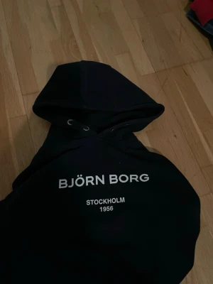 Mörkblå Björn Borg dress  - Snygg dress  från Björn Borg med vit text på bröstet där det står 'BJÖRN BORG STOCKHOLM 1956'. Klassisk huva med dragsko och mjukt material som känns skönt mot huden. Perfekt för en avslappnad och sportig stil.
