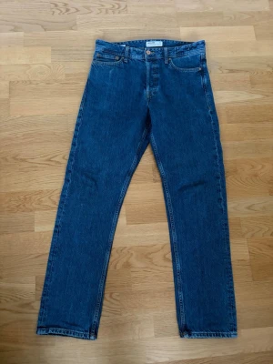 Blå raka jeans från Jack & Jones - Säljer ett par klassiska blå jeans från Jack & Jones med rak passform och fem fickor sitter som ett par regular fit jeans varken slim eller loose men det perfekta emellan. Jeansen har en tidlös look med normalhög midja och är tillverkade i kraftig denim. Perfekta för en clean och stilren outfit. Otroligt fint skick och använda enbart ett fåtal gånger. Storlek W30 L32.