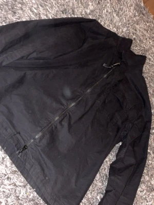C.P. Company jacka  - Snygg svart overshirt med hel dragkedja framtill och en stor bröstficka. Jackan har en enkel och clean design, perfekt att slänga på över en hoodie eller t-shirt. Tillverkad i bomull för en skön känsla och passar till de flesta outfits.