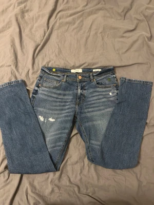 Blå raka jeans från Smog - Säljer ett par klassiska blå jeans från Smog med raka ben och slitna detaljer framtill och baktill. Jeansen har fem fickor, knappgylf. Perfekta för en avslappnad och trendig look.